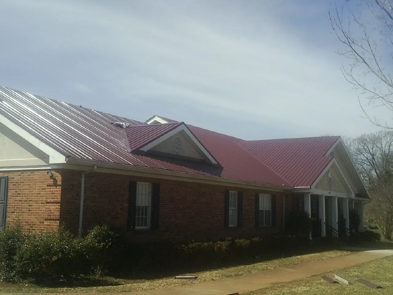 Red metal roof with gabled entries on a long brick building, from a Hail Damage Roof Repair job in Colorado City