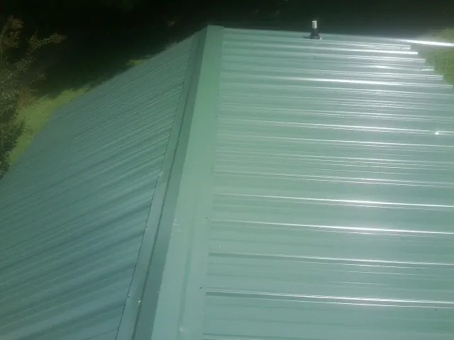 New green metal panels meeting at the ridge of a roof — Flat Roof Repair work by our crew in Colorado City