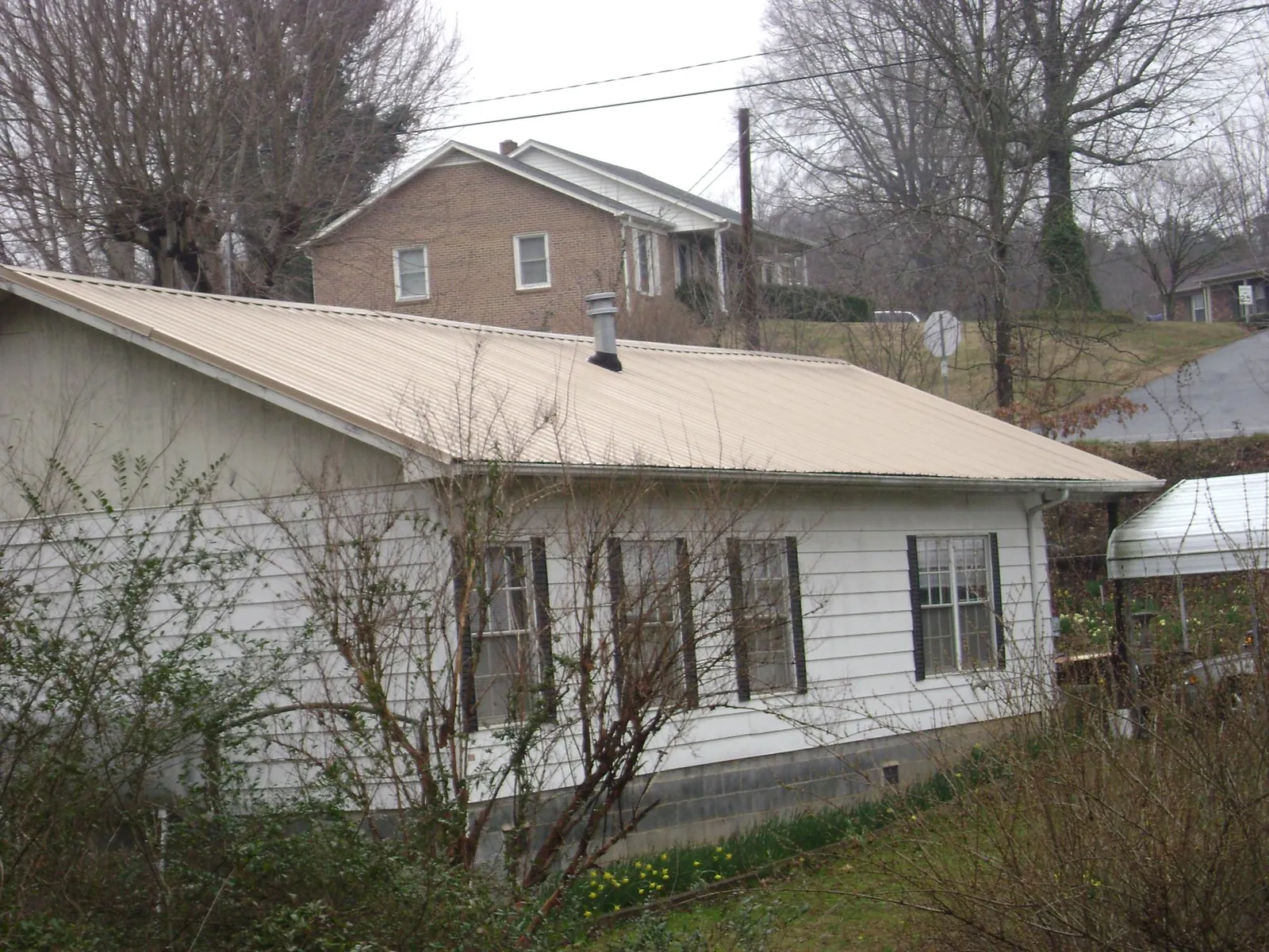Tan metal roof on a white sided house set into a hillside — Commercial Roofing by Roofing Brothers in Colorado City